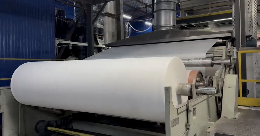 A wide roll of white nonwoven polypropylene web on the winder at the end of the line