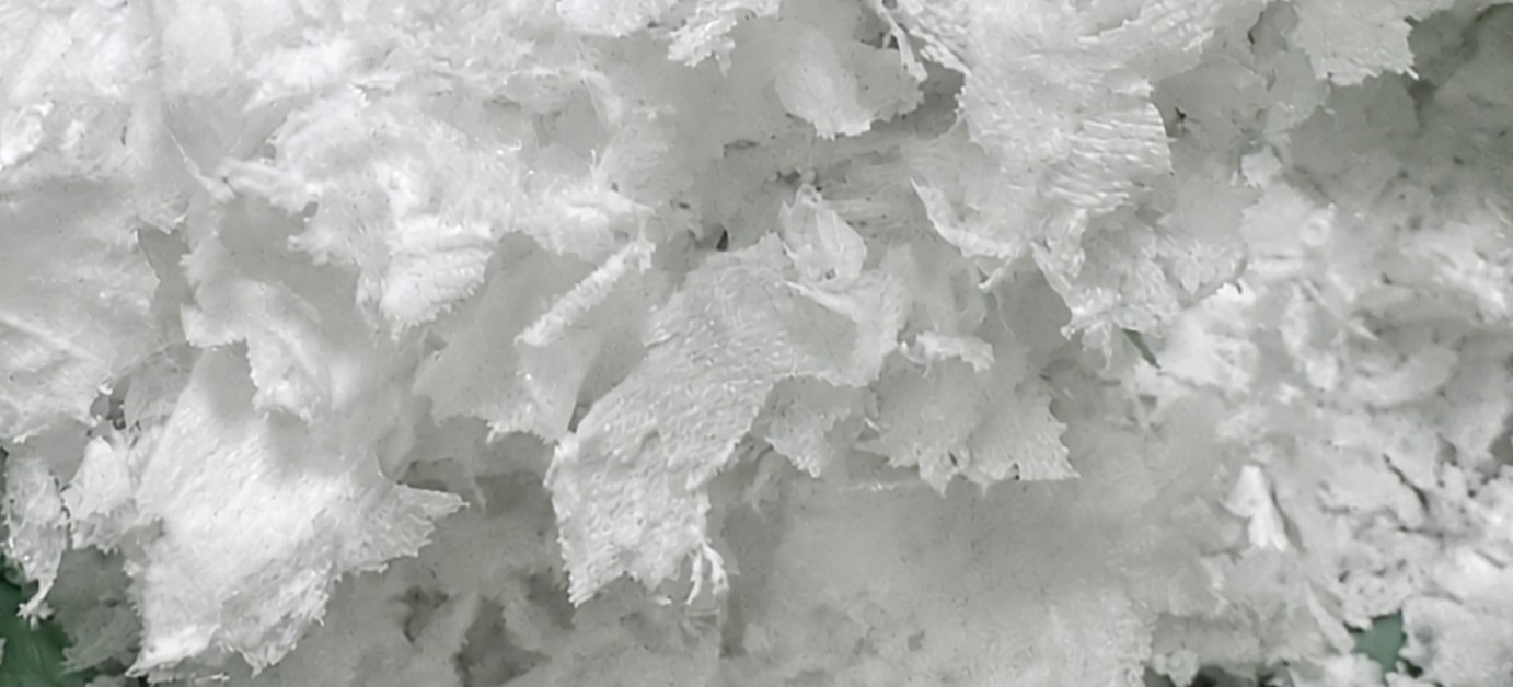 Close-up of loose meltblown polypropylene fill: open, ribbed flakes with visible air space between them